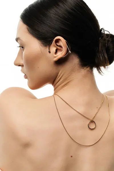 A young brunette woman displays a delicate gold necklace and ear cuff against a white backdrop. — Stock Photo
