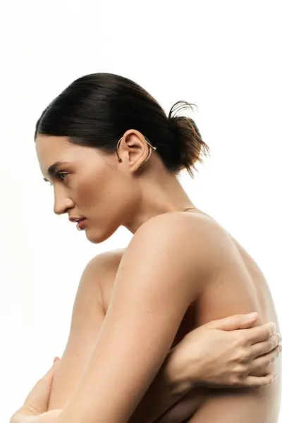 A young brunette woman with her hair pulled back displays a beautiful piece of jewelry on her ear against a white backdrop. — Stock Photo