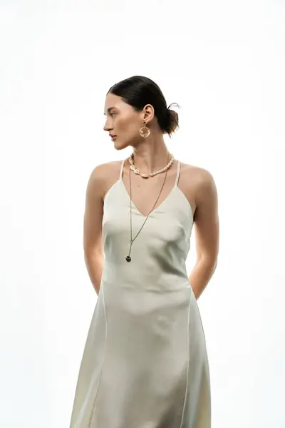 A young woman with long brunette hair wears a white slip dress and showcases beautiful, luxurious jewelry against a clean white background. — Stock Photo