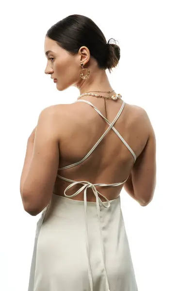 A young woman with long brunette hair poses in a white dress, showcasing her elegant jewelry against a white background. — Stock Photo