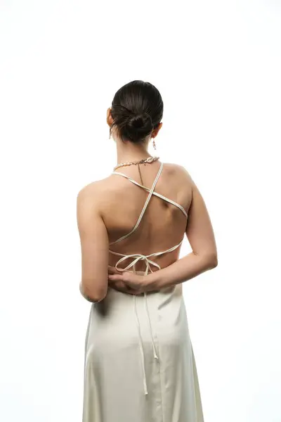 A young brunette woman wearing a white dress with her back to the camera, showing off her beautiful jewelry. — Stock Photo