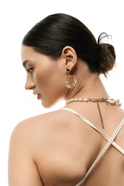 A young brunette woman models beautiful, luxurious jewelry, showcasing a large gold earring and a pearl necklace. — Stock Photo