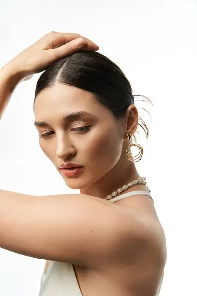 Une jeune femme aux cheveux bruns exhibe d'élégantes boucles d'oreilles en or et un collier de perles sur fond blanc. — Photo de stock