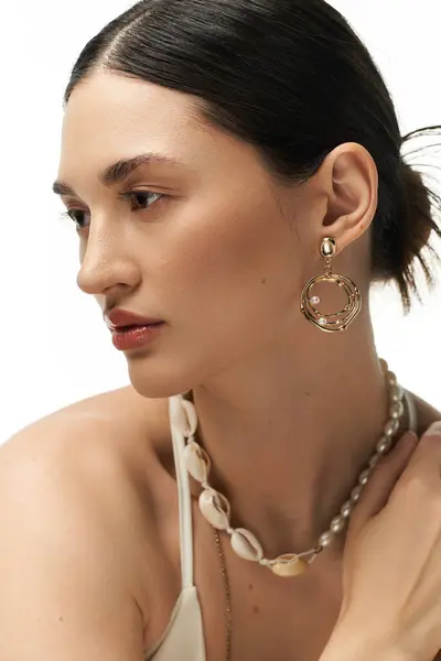 Une jeune femme aux cheveux foncés présente un délicat collier et des boucles d'oreilles sur fond blanc. — Photo de stock