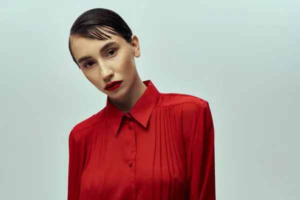 Eine schöne junge Frau mit kurzen Haaren, gekleidet in ein leuchtend rotes Hemd, posiert selbstbewusst vor grauem Hintergrund. — Stockfoto