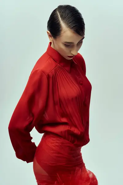 A young woman with short black hair poses in a flowing red dress, exuding confidence and style against a grey backdrop. — Stock Photo