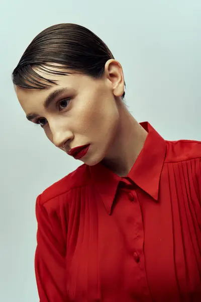 A beautiful young woman with short hair poses in a red blouse, radiating elegance and confidence against a gray backdrop. — Stock Photo