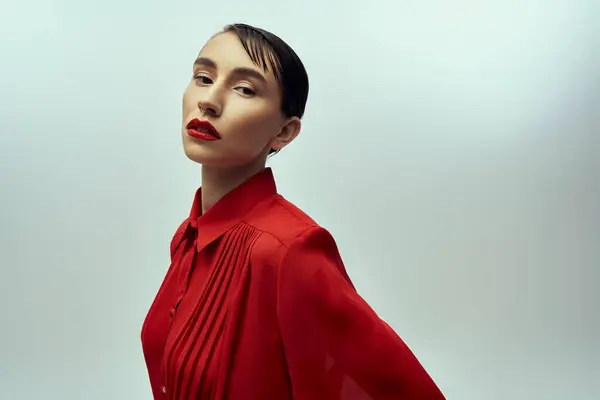 Young woman with short hair in red blouse poses confidently against gray background, creating a striking image. — Stock Photo