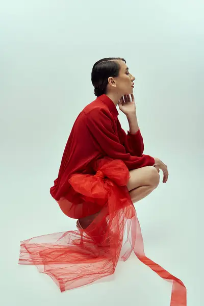 A beautiful young woman with short hair poses in a red outfit against a grey background, showcasing fashion and trends. — Stock Photo