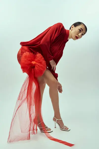 Uma jovem mulher com cabelo curto, vestida de vermelho, posa com uma grande fita vermelha atrás dela. — Fotografia de Stock