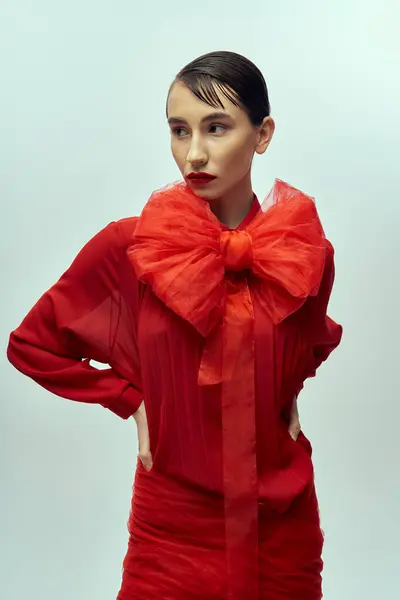 Uma jovem com cabelo curto posa em um vestido vermelho com um grande arco, apresentando um olhar elegante e elegante. — Fotografia de Stock