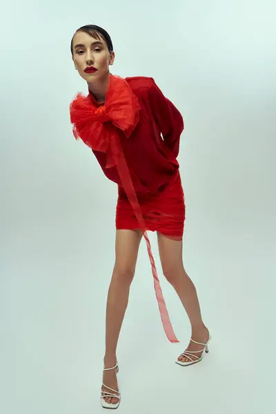A young woman with short hair poses in a red outfit with a large bow. The background is a plain gray. — Stock Photo