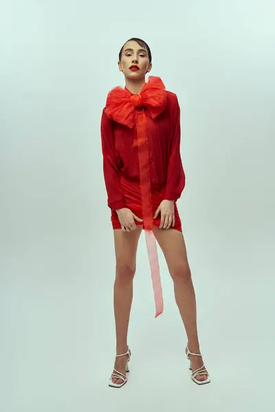 Una joven posa con un vestido rojo y un gran lazo rojo sobre un fondo gris. — Stock Photo