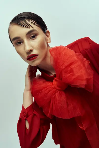 Une jeune femme aux cheveux courts pose dans une robe rouge avec un grand nœud, sur fond gris. — Photo de stock