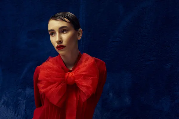 Une jeune femme aux cheveux courts pose sur fond bleu, vêtue d'un chemisier rouge avec un grand nœud. — Photo de stock