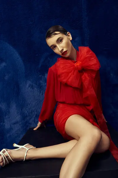 A young woman with short hair poses in a red dress with a large bow against a blue backdrop. — Stock Photo