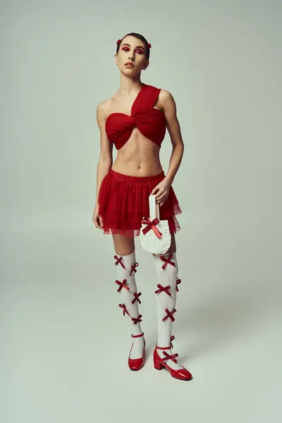 Alluring young woman in red attire with longs socks and bows on grey background — Stock Photo