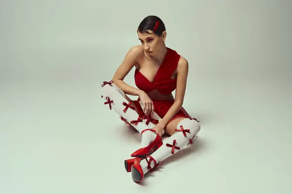 A young woman with short hair poses in a red crop top and mini skirt with red bows on a white background. — Stock Photo
