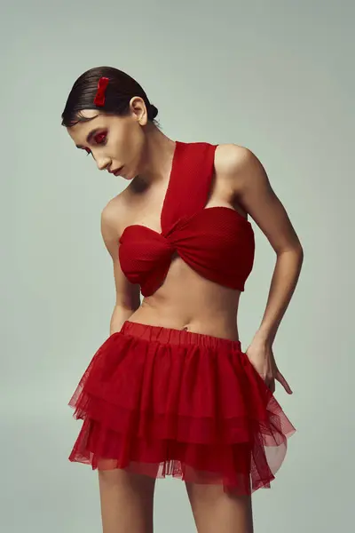 A young woman with short hair poses in a red crop top and mini skirt against a grey background. — Stock Photo