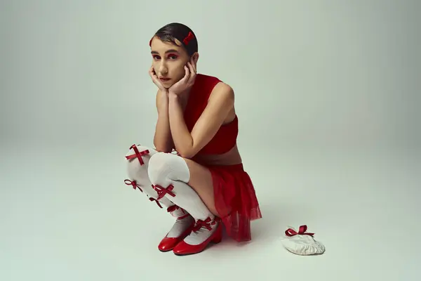 A young woman with short hair poses in a red crop top and mini skirt with bows on a grey background. — Stock Photo