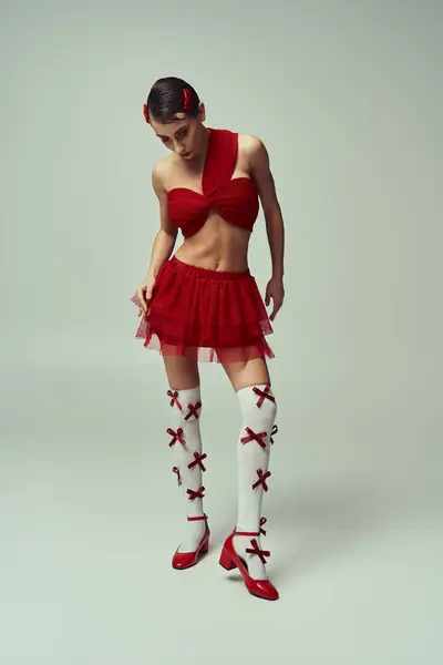 A young woman in a red crop top and mini skirt poses on a grey backdrop. — Stock Photo