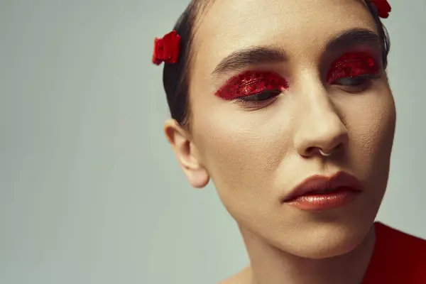Young woman with short hair poses against grey backdrop Bold red eyeshadow, nose piercing. — Stock Photo