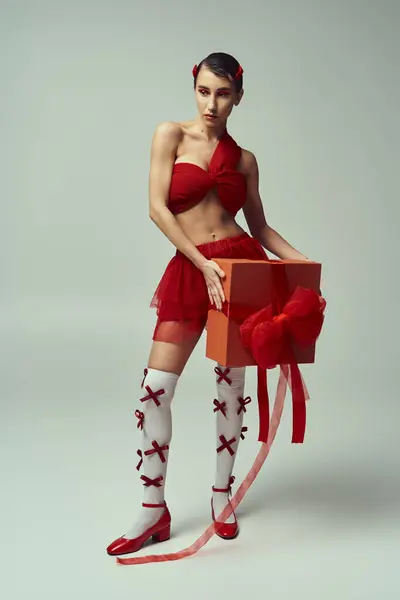 A young woman in a red outfit with a bow holds a large gift box in a studio setting. — Stock Photo