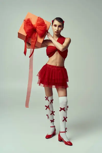 A young woman with short hair, wearing a red outfit and a bow, holds a present in a studio setting. — Stock Photo