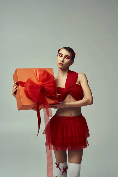 A young woman with short hair, wearing a red outfit with a bow, holds a wrapped gift in a studio setting. — Stock Photo