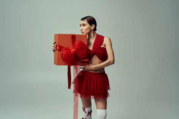 A young woman in a red outfit holds a large gift box with a red bow in a studio setting. — Stock Photo