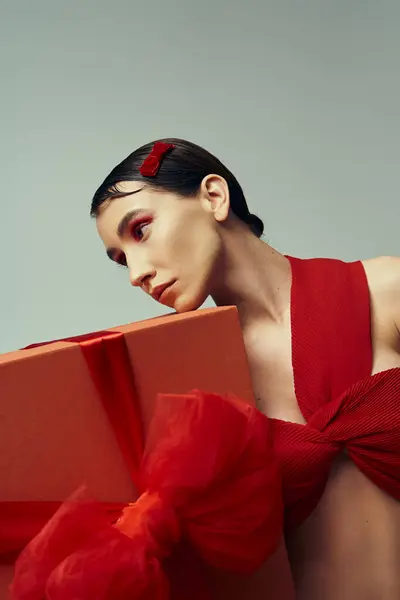 Uma jovem mulher com cabelo curto, vestida com uma roupa vermelha com um arco, segura um presente embrulhado em um estúdio. — Fotografia de Stock