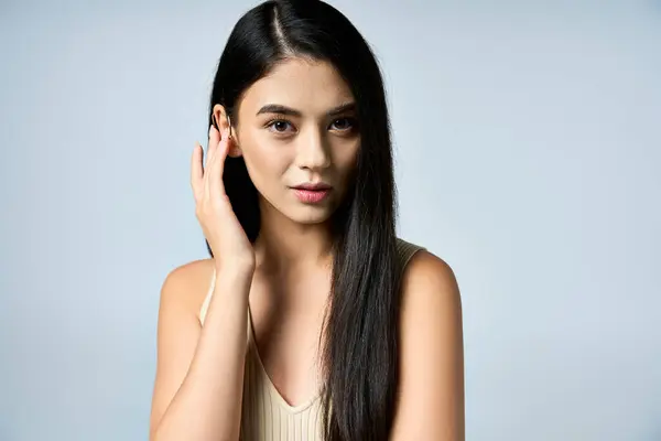 Una giovane donna con lunghi capelli neri posa fiduciosa in uno studio di colore neutro. — Foto stock