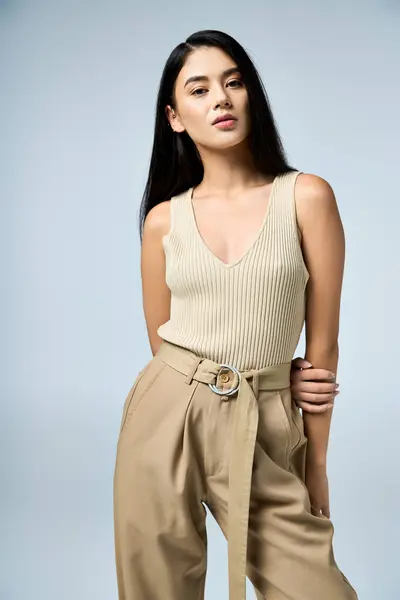 Confident young woman in beige tank top and khaki pants looks at camera. — Stock Photo