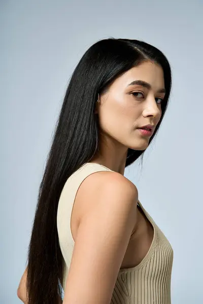 A young woman with long, dark hair poses confidently in a cream-colored tank top. — Stock Photo