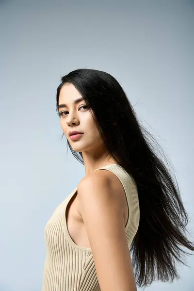 A young woman poses in a studio, her hair flowing in the air, wearing a light-colored tank top. — Stock Photo