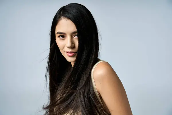 A young woman with long, black hair poses against a light grey background. — Stock Photo