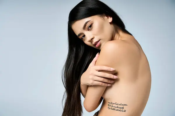 Jovem com longas poses de cabelo preto, exibindo tatuagem de caixa torácica. — Fotografia de Stock