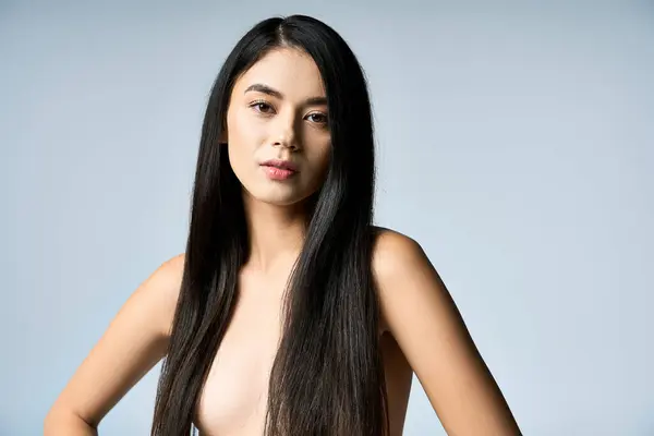 A young woman with long black hair poses confidently against a silver backdrop. — Stock Photo