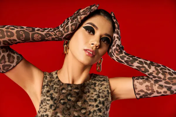 A young woman poses in leopard print gloves against a red backdrop. — Stock Photo