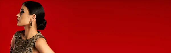 A young woman in a leopard print dress poses against a vibrant red backdrop. — Stock Photo