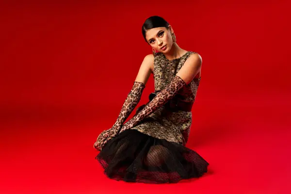 A young woman in a leopard print dress poses against a red background. — Stock Photo