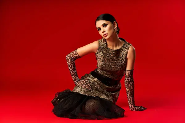 A young woman in a leopard print dress poses on a red background. — Stock Photo