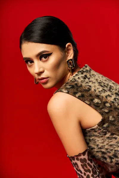 A young woman in a leopard print dress poses against a red background. — Stock Photo