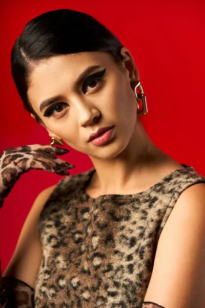 A young woman in a leopard print dress poses against a red background. — Stock Photo