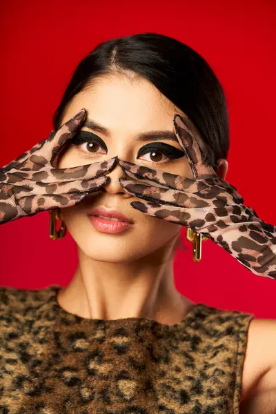 A young woman in a leopard print dress and gloves poses playfully, covering her eyes. — Stock Photo