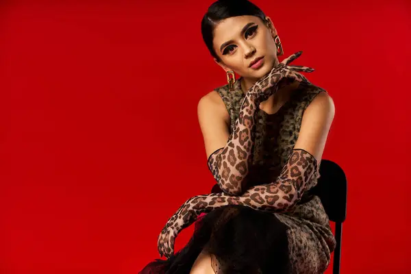 A young woman wearing a leopard print dress and gloves poses against a bright red background. — Stock Photo