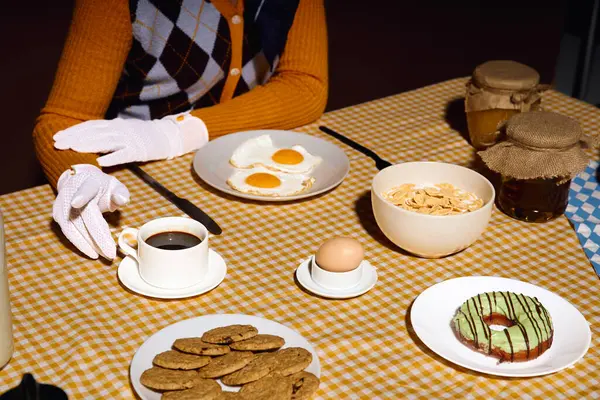 Uma mulher usando luvas brancas senta-se em uma mesa com uma propagação de alimentos para o café da manhã. — Fotografia de Stock