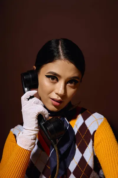 A young woman in a fashionable sweater holds a vintage rotary phone, her expression intriguing. — Stock Photo