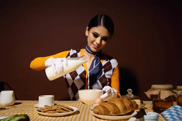 Una joven con un atuendo elegante vierte leche en un tazón en una mesa de desayuno. - foto de stock