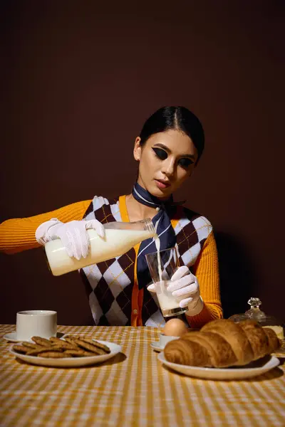Uma jovem mulher em um suéter elegante derrama leite em um copo em uma mesa de café da manhã. — Fotografia de Stock